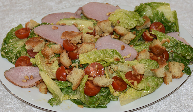 700 g Svinefillet 3 fedd Hvitløk (knuste) Urter (friske) 2 ss Olivenolje 1 ts Sitron 2 hoder Hjertesalat 4 skiver Loff (i terninger) ½ pose Pinjekjerner 200 g Cherrytomater 50 g Parmesan (raspet) Salt, pepper