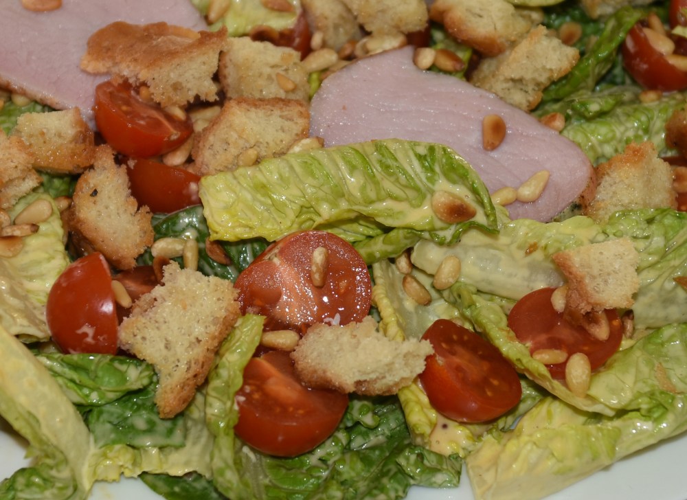 700 g Svinefillet 3 fedd Hvitløk (knuste) Urter (friske) 2 ss Olivenolje 1 ts Sitron 2 hoder Hjertesalat 4 skiver Loff (i terninger) ½ pose Pinjekjerner 200 g Cherrytomater 50 g Parmesan (raspet) Salt, pepper