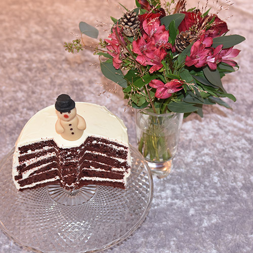 Snømannkake Ingredienser: 450 g Hvetemel (7 ½ dl) 400 g Sukker (5 dl) 4 ss Maisenna (70 g) 4-5 ss Kakao (70 g) 1 ss Natron 1 ts Bakepulver 4 Egg 3 dl Rømme 3 ½ dl Vann (varmt) 1 dl Olje (nøytral) 1 ts Vaniljeekstrakt 1 ts Eddik (eplesider) 2 ss Konditorfarge (rød) Fyll og topping: 500 g Kremost (Philadelphia) 225 g Smør 600 g Melis 1 ts Vaniljeekstrakt Pynt: Marsipansnømann Snømannkjeks