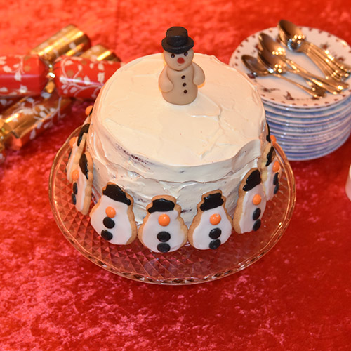 Snømannkake Ingredienser: 450 g Hvetemel (7 ½ dl) 400 g Sukker (5 dl) 4 ss Maisenna (70 g) 4-5 ss Kakao (70 g) 1 ss Natron 1 ts Bakepulver 4 Egg 3 dl Rømme 3 ½ dl Vann (varmt) 1 dl Olje (nøytral) 1 ts Vaniljeekstrakt 1 ts Eddik (eplesider) 2 ss Konditorfarge (rød) Fyll og topping: 500 g Kremost (Philadelphia) 225 g Smør 600 g Melis 1 ts Vaniljeekstrakt Pynt: Marsipansnømann Snømannkjeks