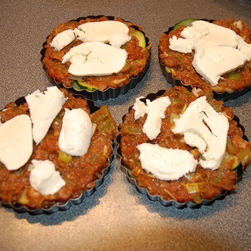 Squash – og tomatpai Ingredienser: 4 Poteter 1 Squash 1 Løk 1 Paprika (grønn) ¼ Purre (ca. 50 g) 1 fedd Hvitløk 1 ts Spisskumen 1 ts Paprikapuver 2 ss Basilikum (hakket) 1 ts Persile (hakket) 1 bx Tomater (hermetiske) 1 Mozzarella Salt og pepper 60 g Strøbrød 2 ss Parmesan 4 Terteformer (små, med løs bunn) Eller noe annet å steke dem i