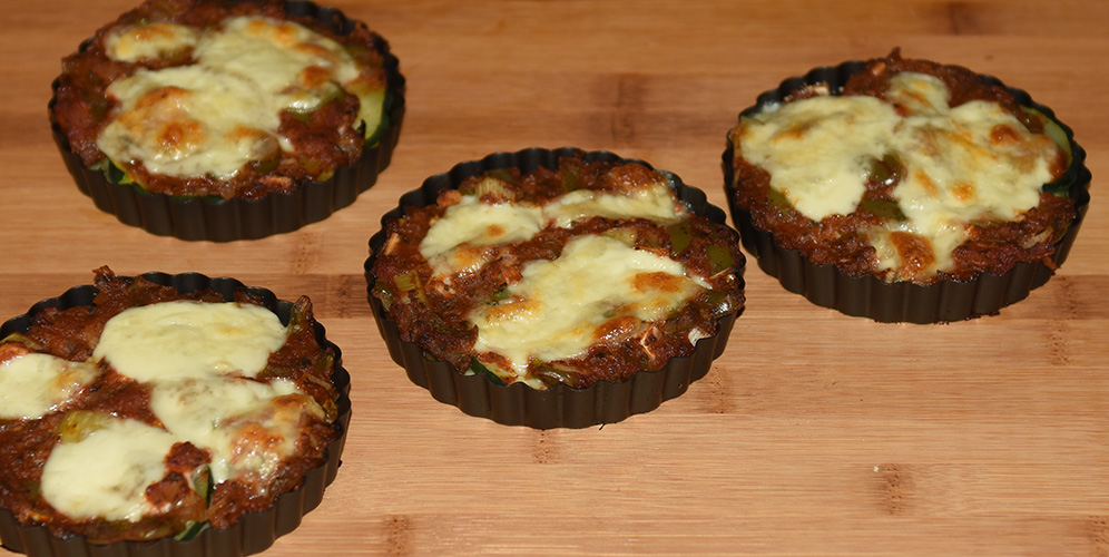 Squash – og tomatpai Ingredienser: 4 Poteter 1 Squash 1 Løk 1 Paprika (grønn) ¼ Purre (ca. 50 g) 1 fedd Hvitløk 1 ts Spisskumen 1 ts Paprikapuver 2 ss Basilikum (hakket) 1 ts Persile (hakket) 1 bx Tomater (hermetiske) 1 Mozzarella Salt og pepper 60 g Strøbrød 2 ss Parmesan 4 Terteformer (små, med løs bunn) Eller noe annet å steke dem i