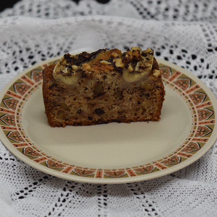 KRISTINS BANANBRØD Ingredienser: 2 ½ dl Hvetemel 2 ts Bakepulver 1 ts Vaniljesukker 1 ts Kardemomme (valgfritt) 2 Egg 1 ½ dl Sukker 50 g Smør 1 dl Melk 40 g Kokesjokolade (mørk, hakket) 40 g Valnøtter 2 Bananer (godt modne, gjerne med brune flekker) Topping: 10 g Kokesjokolade (mørk, hakket) 10 g Valnøtter 1 Banan