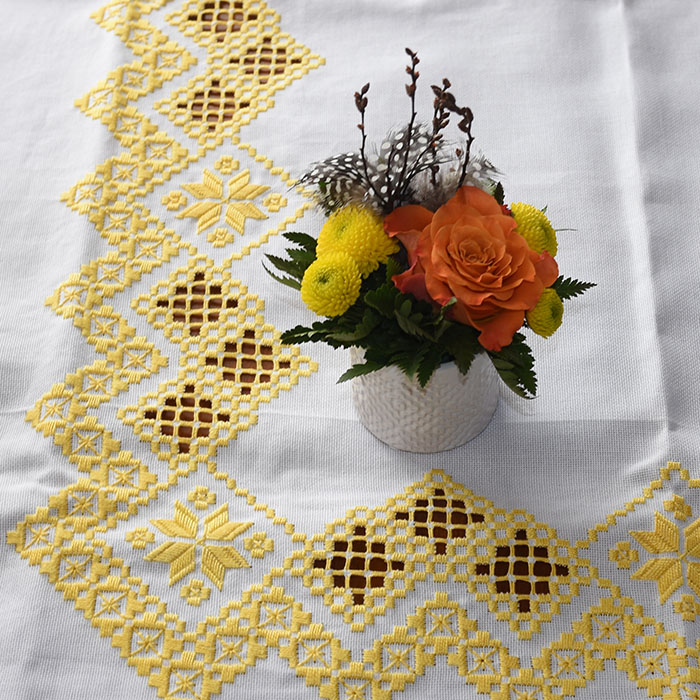 Liten Oppsats med gule og oransje blomster på gul påskeduk, sydd med Hardangersøm