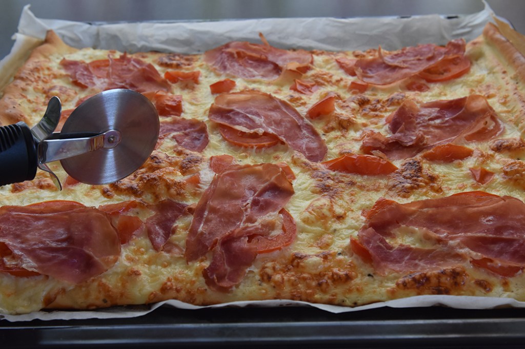 Hvit pizza med spekeskinke, ruccula  Ingredienser:  Pizzabaunn:  1 ss	Sukker 2 ts	Tørrgjær 2 dl 	Vann (ca 36 grader) 450 g	Hvetemel ½ ts 	Salt  3 ss	Olje (oliven)  Fyll og topping 1 bx	Rømme (gjerne lett) 2 fedd	 Hvitløk 150 g	Ost (hvit, raspet) 2 	Tomater (skivet) 9 skiver	Spekeskinke 1 pk	Rucculoa