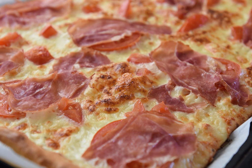 Hvit pizza med spekeskinke og ruccula  Ingredienser:  Pizzabaunn:  1 ss	Sukker 2 ts	Tørrgjær 2 dl 	Vann (ca 36 grader) 450 g	Hvetemel ½ ts 	Salt  3 ss	Olje (oliven)  Tips! La deigen heve i kjøleskapet, da tar det ca. 8 timer. Dekk bollen med plast før du setter den inn.  Fyll og topping 1 bx	Rømme (gjerne lett) 2 fedd	 Hvitløk 150 g	Ost (hvit, raspet) 2 	Tomater (skivet) 9 skiver	Spekeskinke 1 pk	Rucculoa