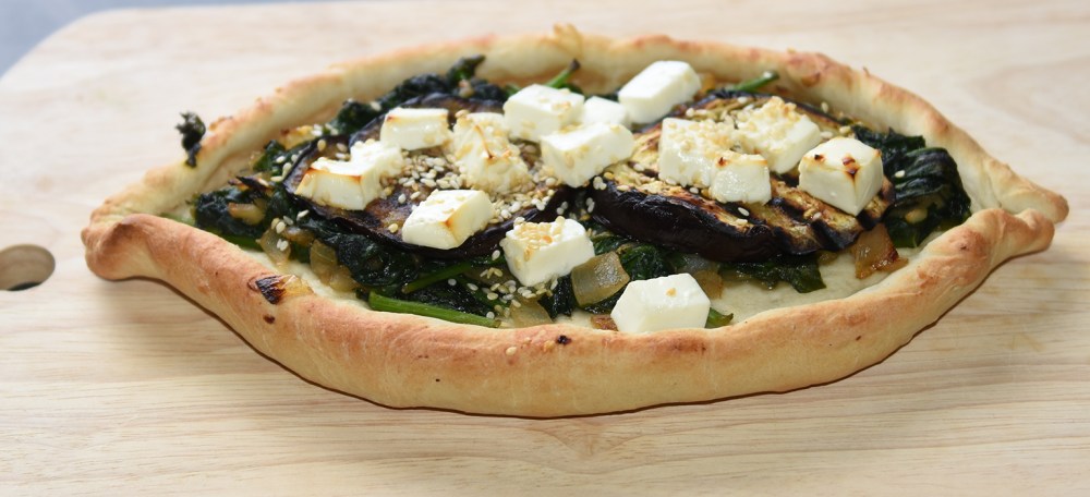 Ingredienser: Bunn: ½ pk Gjær 1 ts Sukker 300 g Hvetemel 2 ts Salt 2 ss Olje (oliven) ca. 1 ½ dl Vann (fingervarmt) Topping: 1 Aubergine (skivet) 1 Løk (skivet) 2 fedd Hvitløk 1 pk Babyspinat 150 g Fetaost 1 ss Sesamfrø