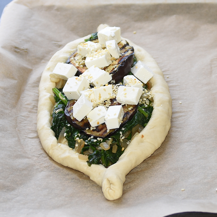 Ingredienser:  Bunn:  ½ pk	Gjær 1 ts	Sukker 300 g	Hvetemel 2 ts	Salt 2 ss	Olje (oliven) ca. 1 ½ dl	Vann (fingervarmt)  Topping: 1	Aubergine (skivet) 1 	Løk (skivet) 2 fedd	Hvitløk 1 pk	Babyspinat 150 g	Fetaost 1 ss	Sesamfrø